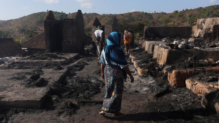 Warga melintasi reruntuhan gerbang dan bangunan adat Desa Sade pascakebakaran di Lombok Tengah, NTB