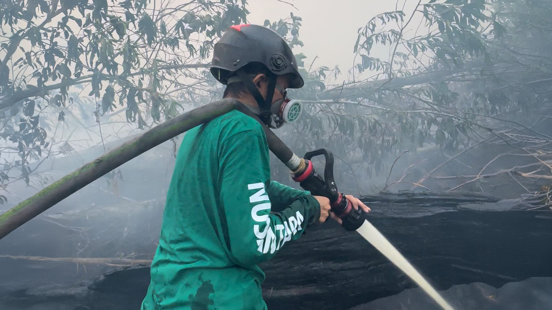 Anggota Relawan Nusantara bersama petugas Damkar bahu-membahu membawa selang di lokasi pemadaman kebakaran lahan.