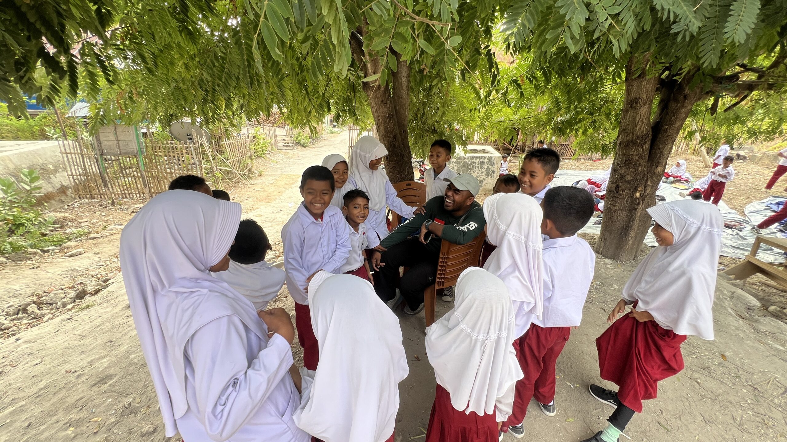 Relawan Nusantara berinteraksi dan mengajar siswa SD di bawah pepohonan dalam program sekolah darurat NTT.